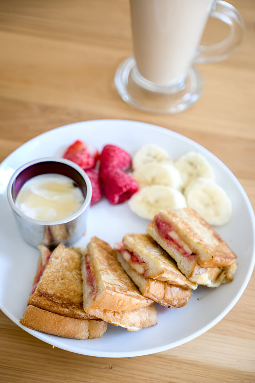 A plate of French toast with a side of strawberries, raspberries, and banana slices, accompanied by a small cup of syrup.