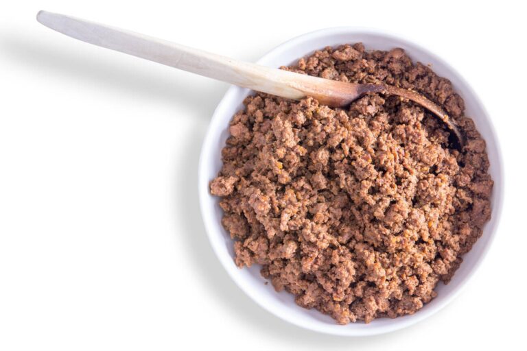 A bowl of ground meat with a wooden spoon resting on the edge.