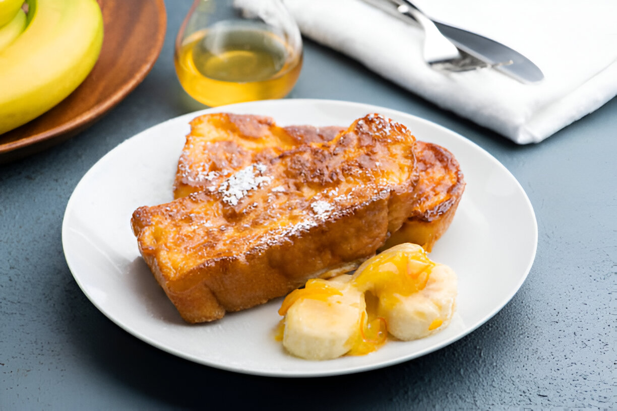 A plate of French toast served with banana slices and a drizzle of syrup.
