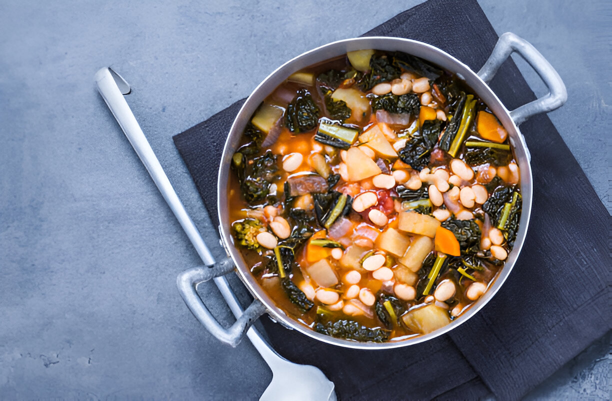 A pot of vegetable and bean soup on a black napkin with a metal spoon.