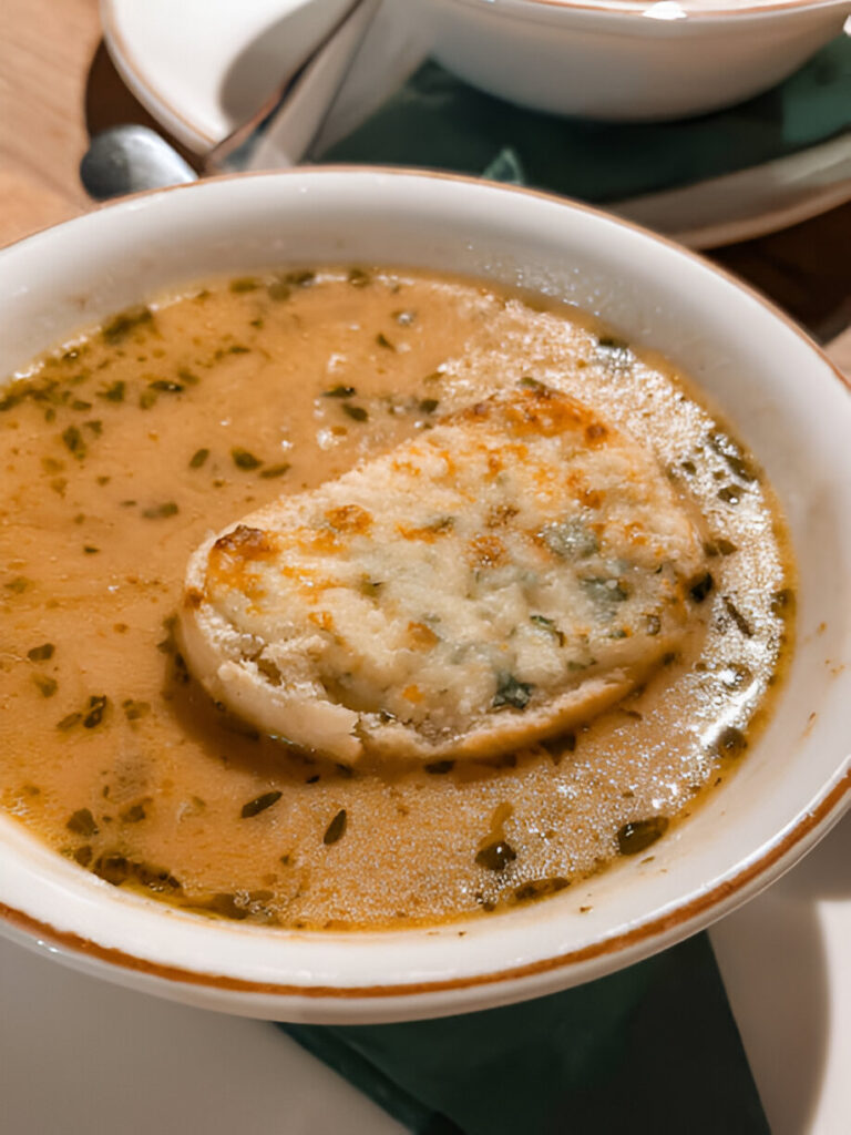 A bowl of hot soup with a piece of toasted bread on top, garnished with herbs.