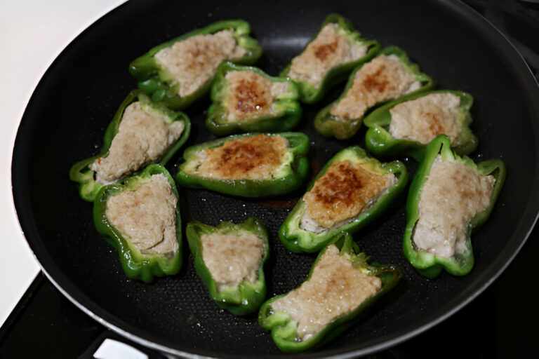 Stuffed green peppers cooking in a frying pan.