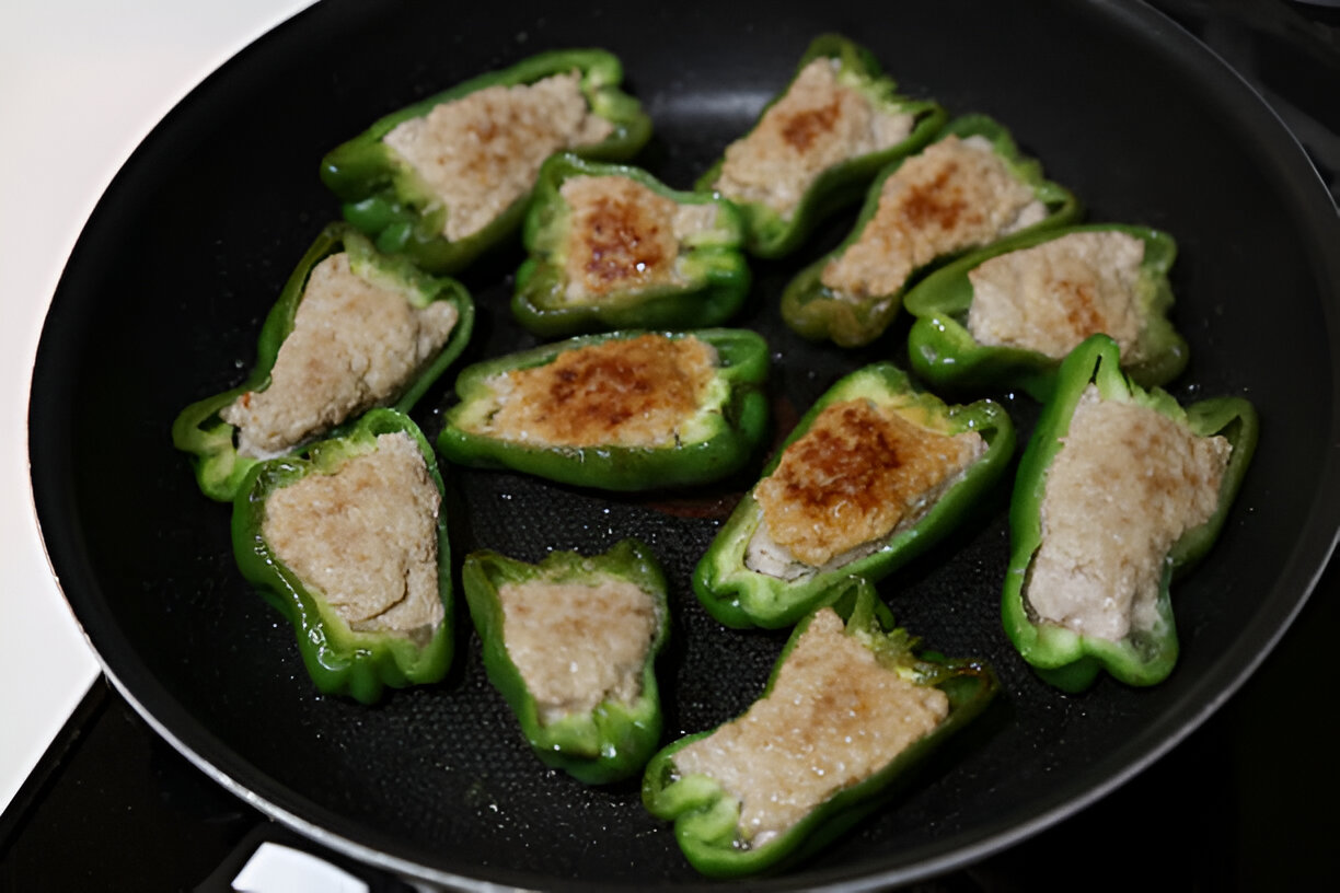 Stuffed green peppers cooking in a frying pan.