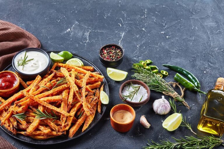 A platter of crispy sweet potato fries served with dipping sauces, garnished with lime and fresh herbs