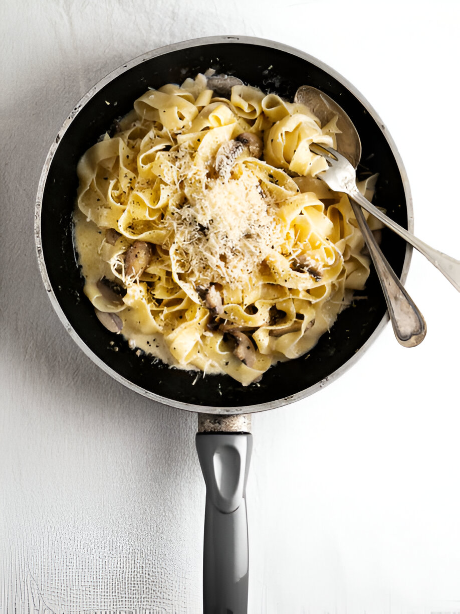A pan filled with creamy fettuccine pasta topped with grated cheese and mushrooms.