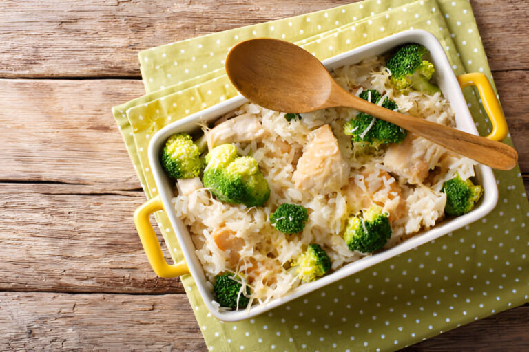 A casserole dish filled with chicken, rice, and broccoli on a wooden table.