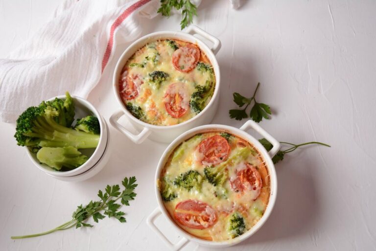 Two individual servings of baked broccoli and tomato dish in white ramekins with a side of broccoli and fresh parsley.