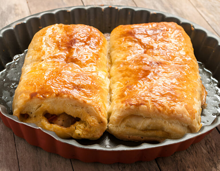 Two golden-brown pastries in a round metal baking dish on a wooden surface