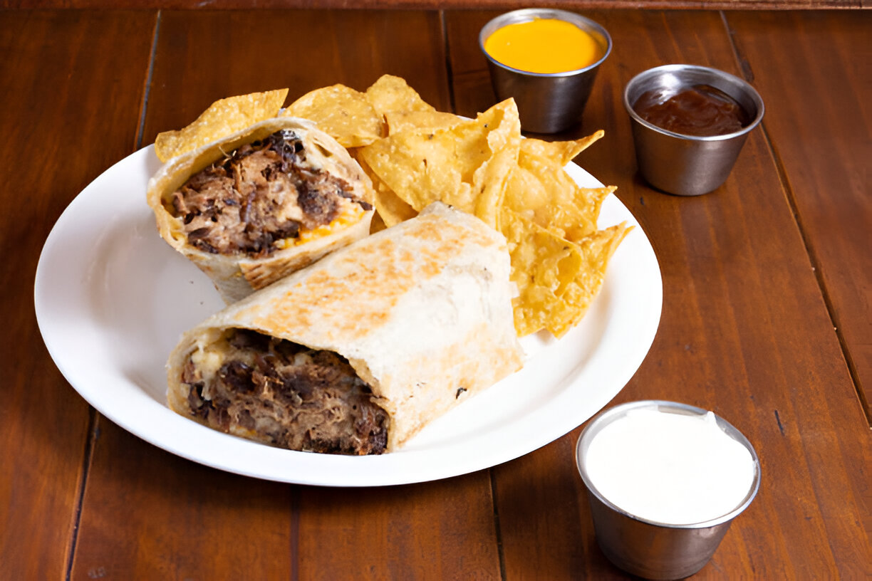 A plate with two burritos, tortilla chips, and three dipping sauces.