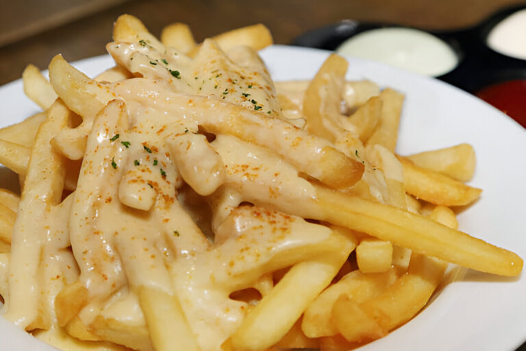 Plate of fries topped with a creamy sauce and sprinkled with seasoning.