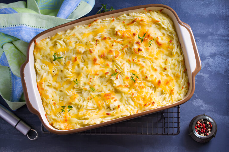 Baked creamy potato casserole topped with melted cheese and fresh herbs, served in a ceramic dish on a cooling rack.