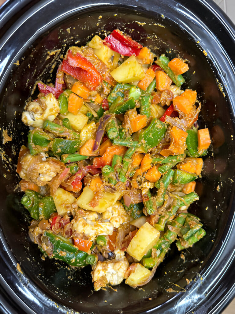A colorful vegetable medley cooked in a slow cooker, featuring vibrant bell peppers, carrots, green beans, and chunks of potatoes, all coated in a rich sauce.