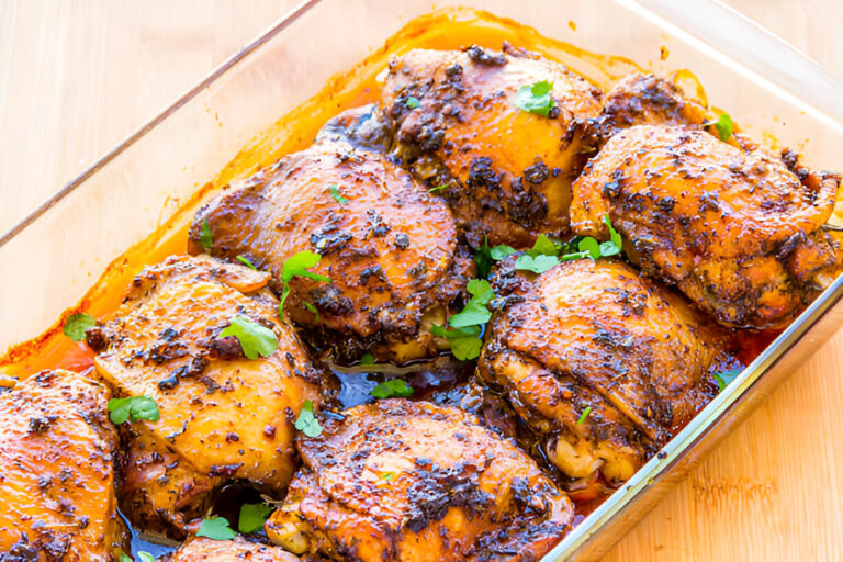 A close-up view of a dish containing seasoned roasted chicken thighs garnished with fresh herbs.