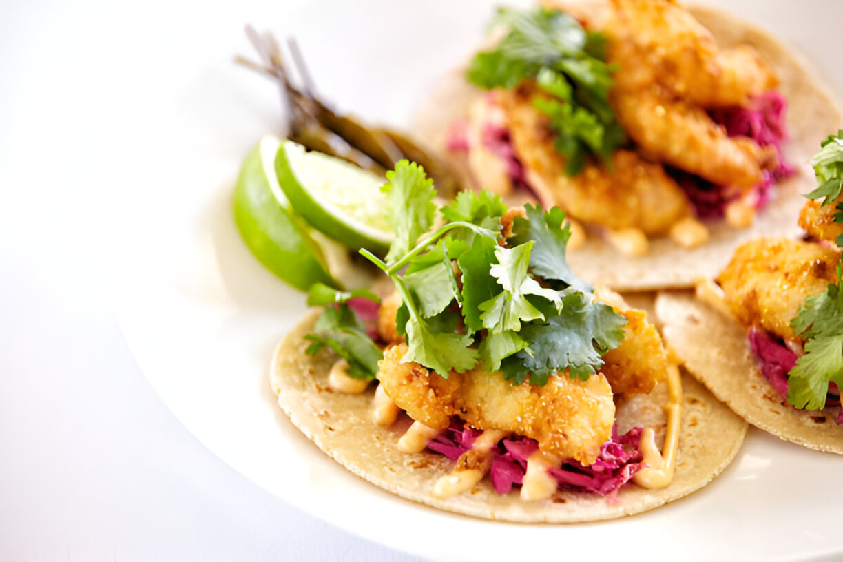 Three delicious shrimp tacos topped with cilantro and served with lime and pickled vegetables.