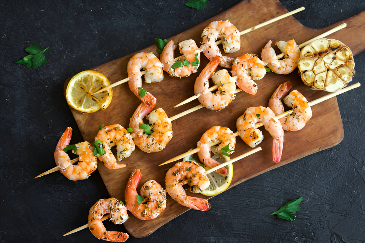 Grilled shrimp skewers with lemon and herbs on a wooden cutting board