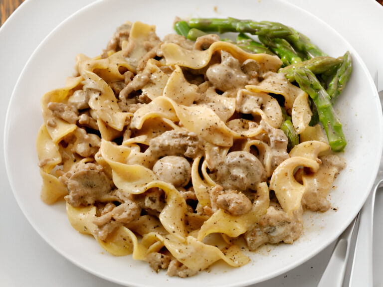 A plate of egg noodles mixed with creamy meat sauce and served with asparagus.