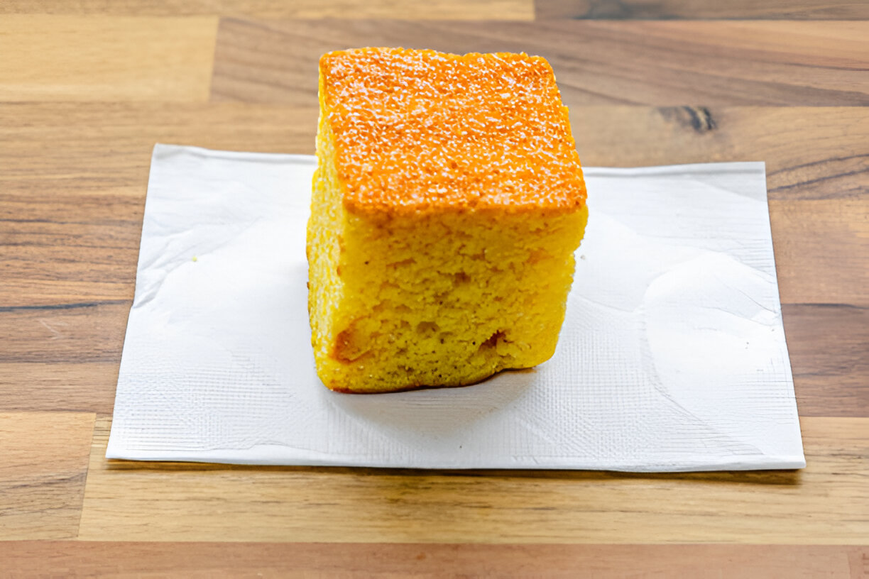 A cube-shaped yellow cake on a white paper napkin, placed on a wooden table.