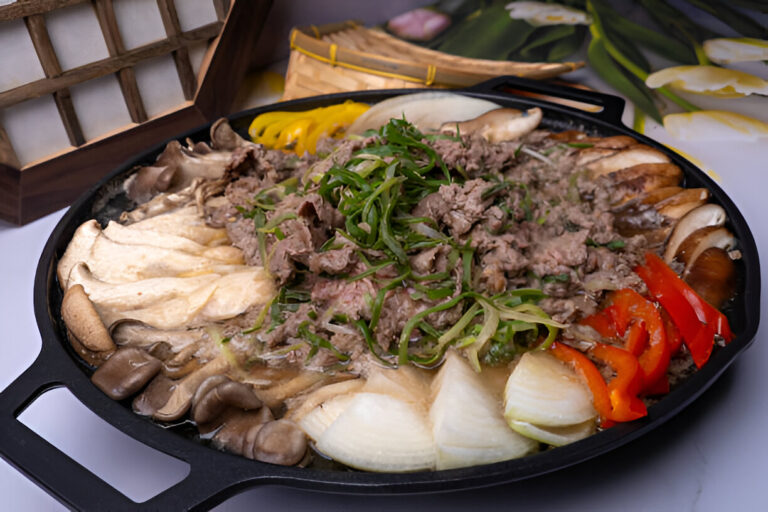 A sizzling pot of beef and assorted mushrooms garnished with green onions and red bell peppers, presented on a black cast iron skillet.