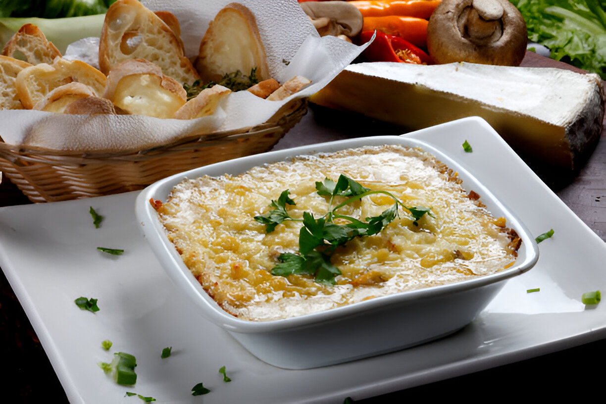 A dish of baked cheesy goodness served in a white bowl, garnished with fresh cilantro, alongside a basket of bread.