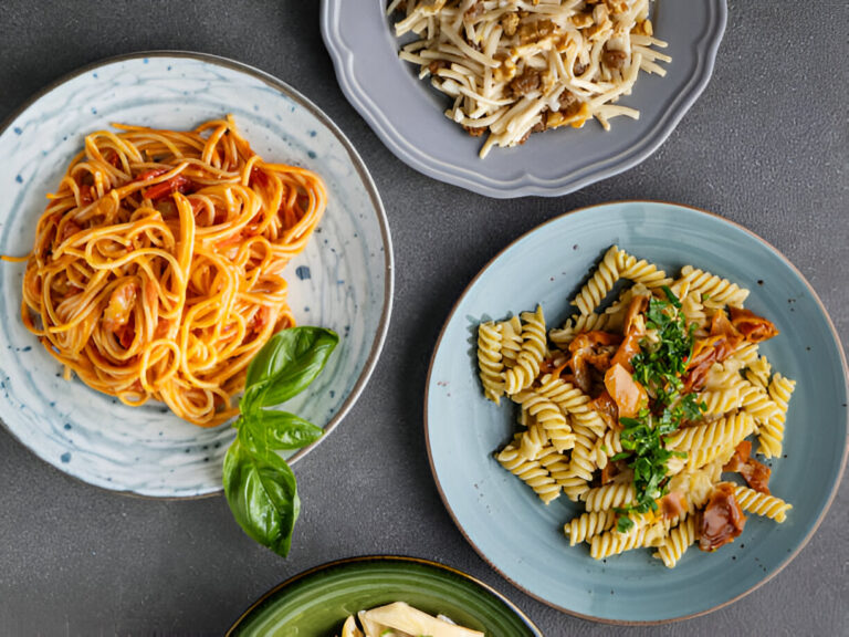 Three plates of pasta dishes with different sauces and garnishes on a gray surface