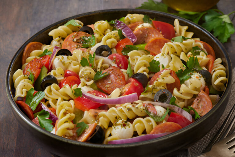 A delicious bowl of pasta salad with rotini noodles, sliced pepperoni, olives, tomatoes, and herbs.