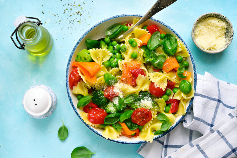 A vibrant bowl of pasta with colorful vegetables, including cherry tomatoes, green peas, and basil, served on a blue background.