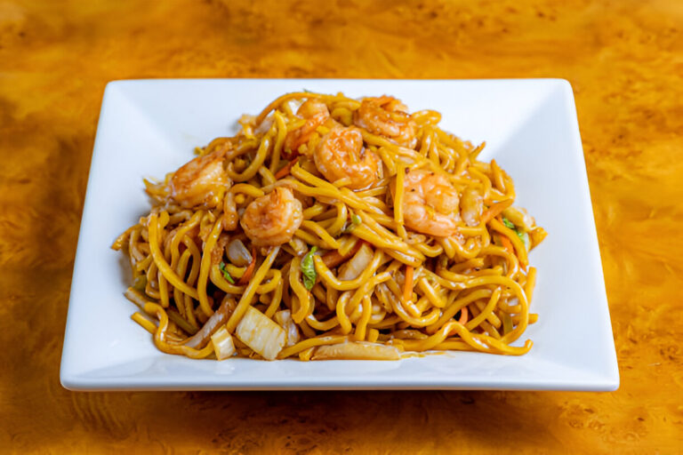 A plate of shrimp lo mein featuring golden noodles mixed with shrimp and vegetables, served on a white square dish.