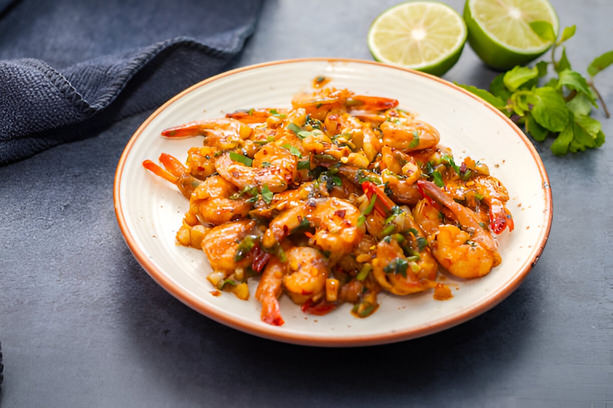 A plate of shrimp sautéed with vegetables and garnished with herbs, served with lime halves.