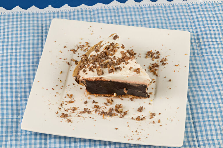A slice of chocolate pie topped with whipped cream and crumbled nuts on a white plate.