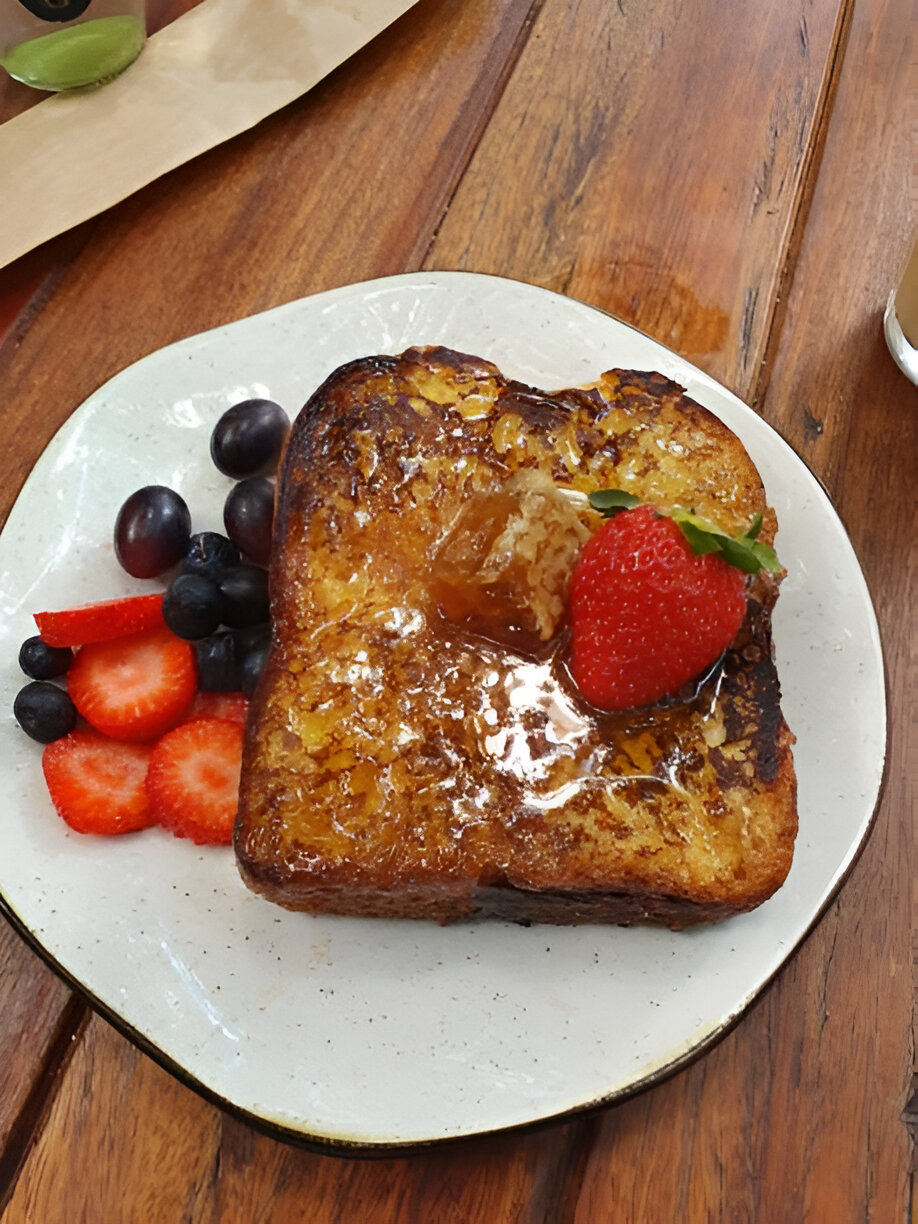 A plate of French toast topped with a strawberry and syrup, accompanied by fresh berries.