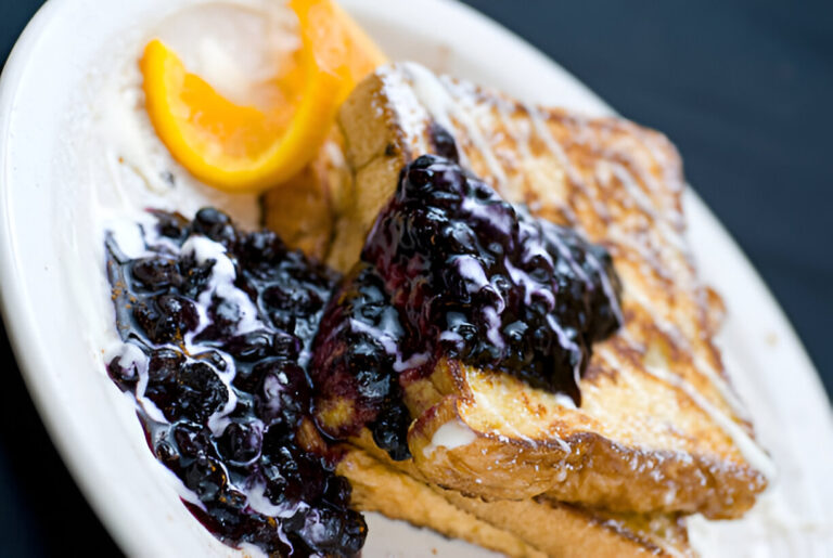 A plate of French toast topped with blueberry jam and a slice of lemon.