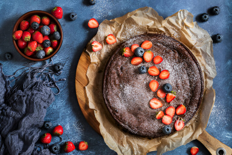 A delicious chocolate cake topped with strawberries and blueberries, placed on a wooden board with parchment paper.