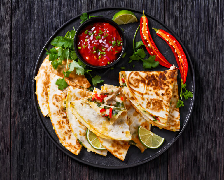 A plate of quesadillas with red salsa, lime, and fresh herbs.