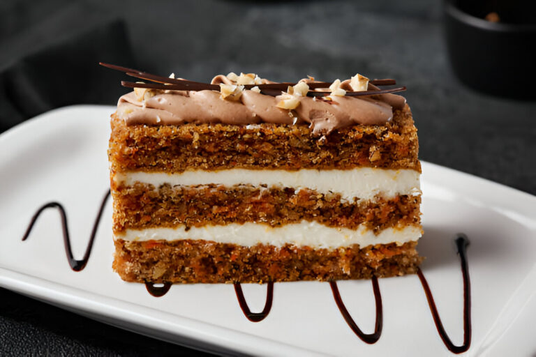 A slice of layered cake with cream filling and chocolate frosting, garnished with chocolate curls and nuts on a white plate.