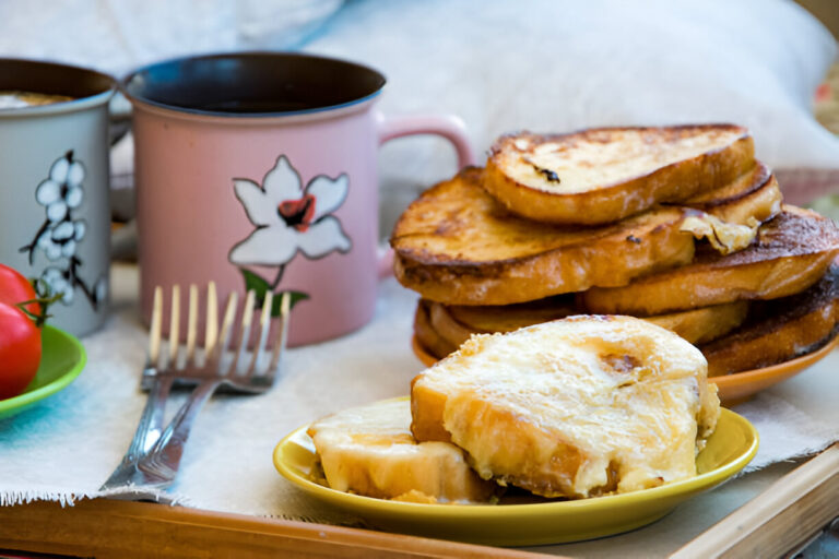 Breakfast scene with two cups of coffee, a plate of French toast, and fresh tomatoes on a tray.