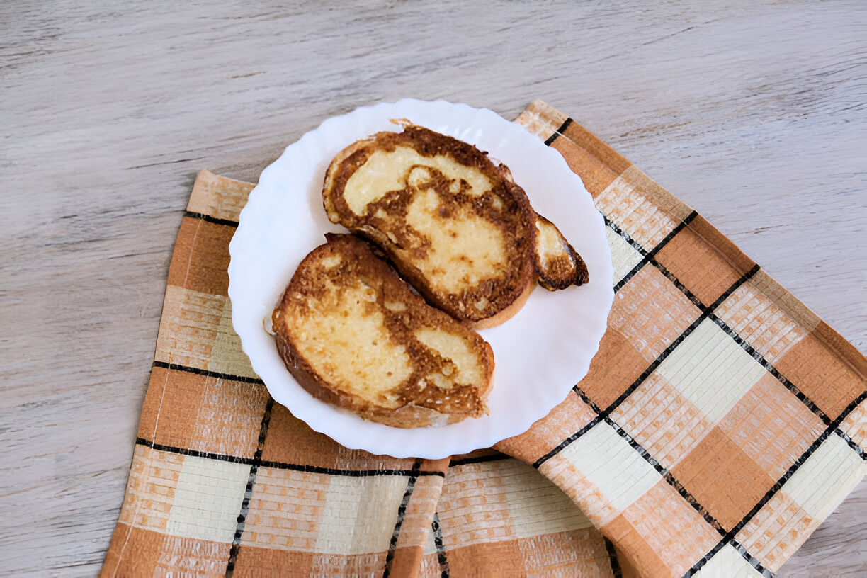 Two slices of toasted French toast on a white plate, placed on a plaid tablecloth.