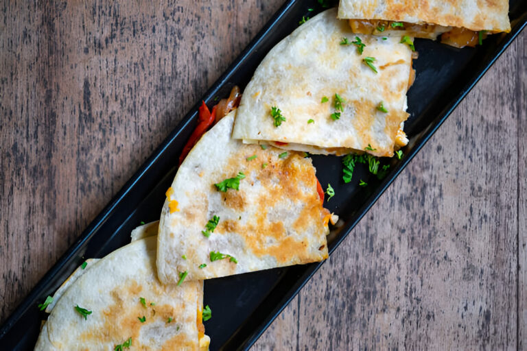 A close-up of sliced quesadillas on a black plate, garnished with chopped parsley on a wooden table.