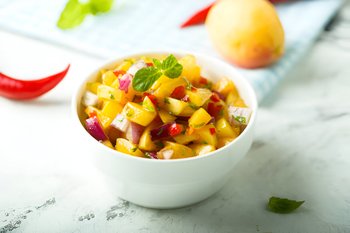 A fresh, colorful fruit salsa in a white bowl featuring diced mango, red onion, and red pepper garnished with mint leaves.
