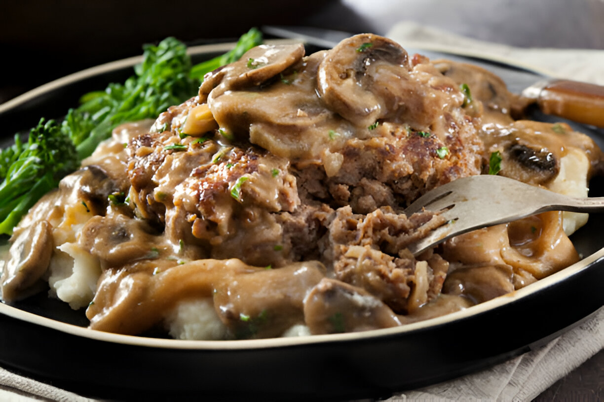 A plate of meatloaf topped with mushroom gravy served with mashed potatoes and green vegetables.