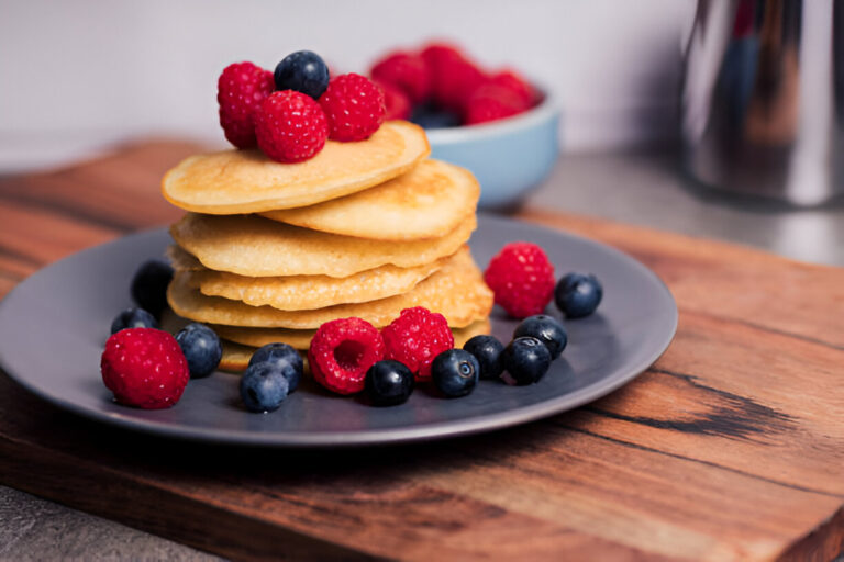 A stack of pancakes topped with fresh raspberries and blueberries on a gray plate