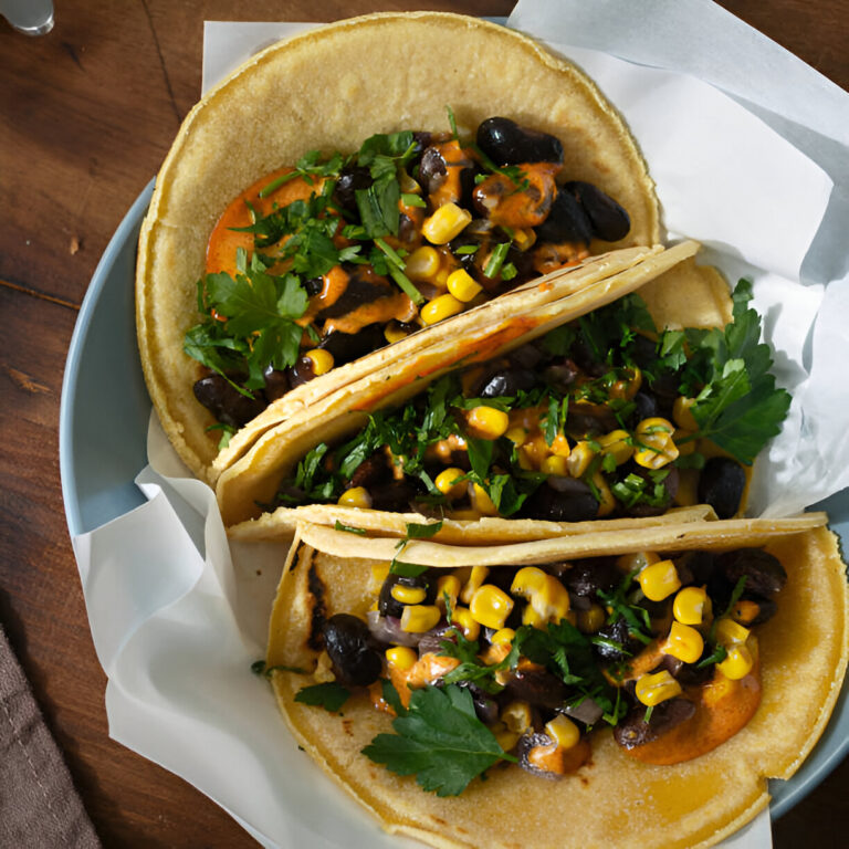 Three tacos filled with black beans, corn, and fresh herbs on a blue plate