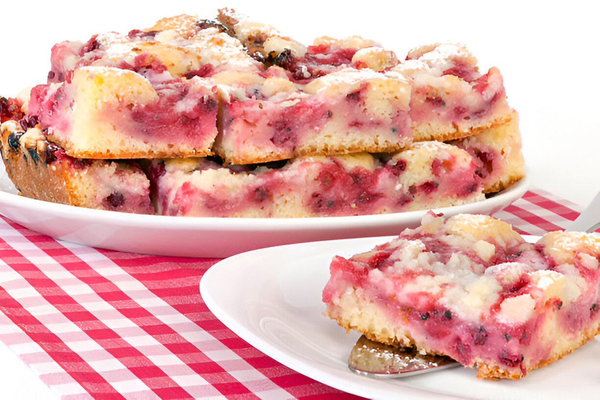 A slice of berry dessert on a white plate next to a larger portion of the dessert on a serving dish.
