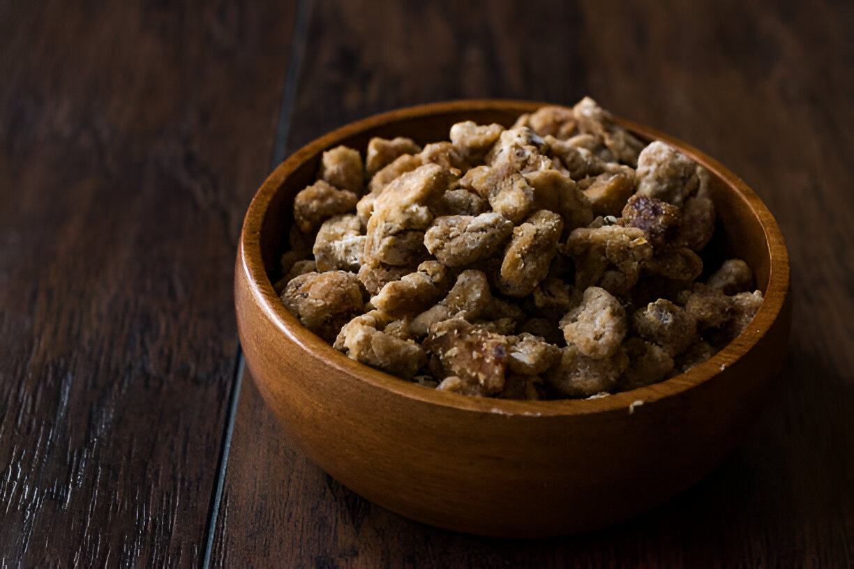 A wooden bowl filled with crunchy snacks on a dark wooden surface