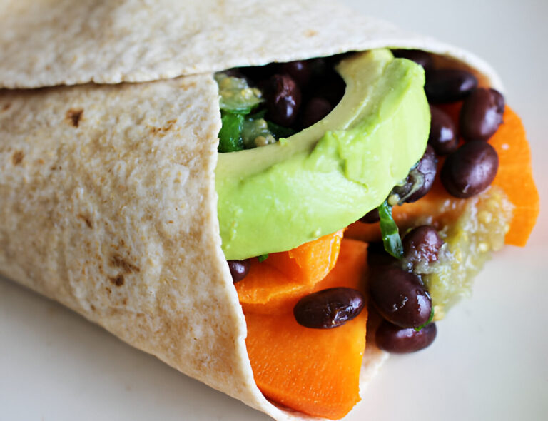 A close-up of a whole wheat wrap filled with avocado, black beans, and orange vegetables.