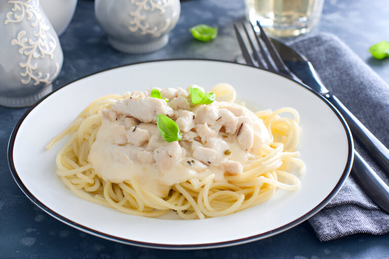 Plate of spaghetti topped with creamy chicken sauce and fresh basil leaves