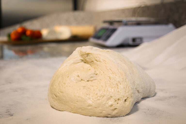 A mound of dough resting on a floured kitchen countertop with ingredients in the background.