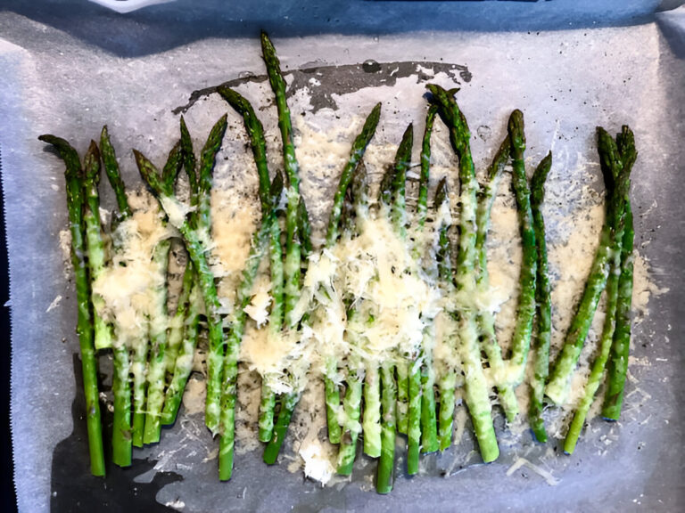 Roasted asparagus sprinkled with cheese on a baking tray lined with parchment paper