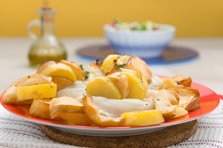 A colorful dish featuring roasted potatoes and fish, served on a red plate with a salad in the background.