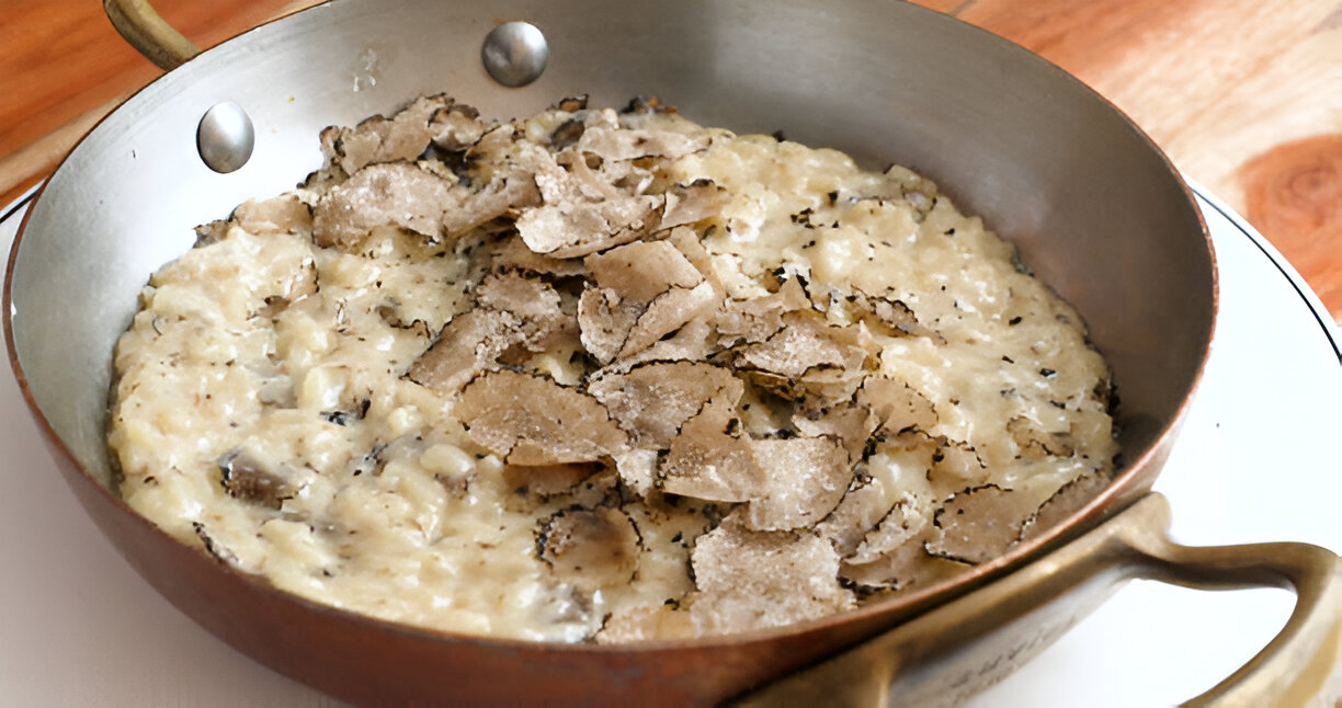 A luxurious dish of risotto topped with thinly sliced truffles in a copper pan.