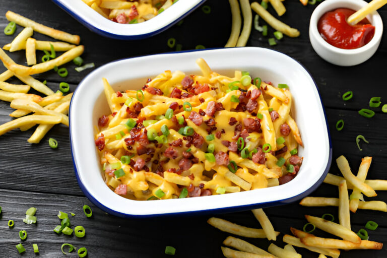 A close-up of a dish featuring French fries topped with cheese, bacon bits, and green onions, served in a white dish. Surrounding the dish are scattered fries and a small bowl of ketchup.